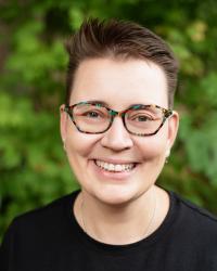 Portrait photo of Karoliina with short hair and colorful glasses, smiling and wearing a black shirt.