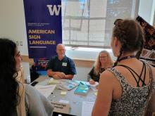 Lance Forshay and Kritsit Winter talk to students at the World Language Fair people standing and sitting at a table