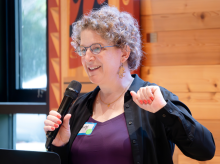 Emily Bender holding a microphone giving a speech