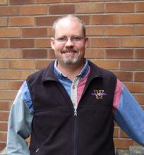 Professor Forshay standing in front a brick wall, smiling.