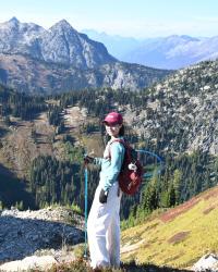 image of a woman hiking through the mountains, she appears in the foreground with the mountain range behind her.