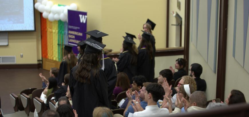 Audience clapping for standing graduates in caps and gowns.
